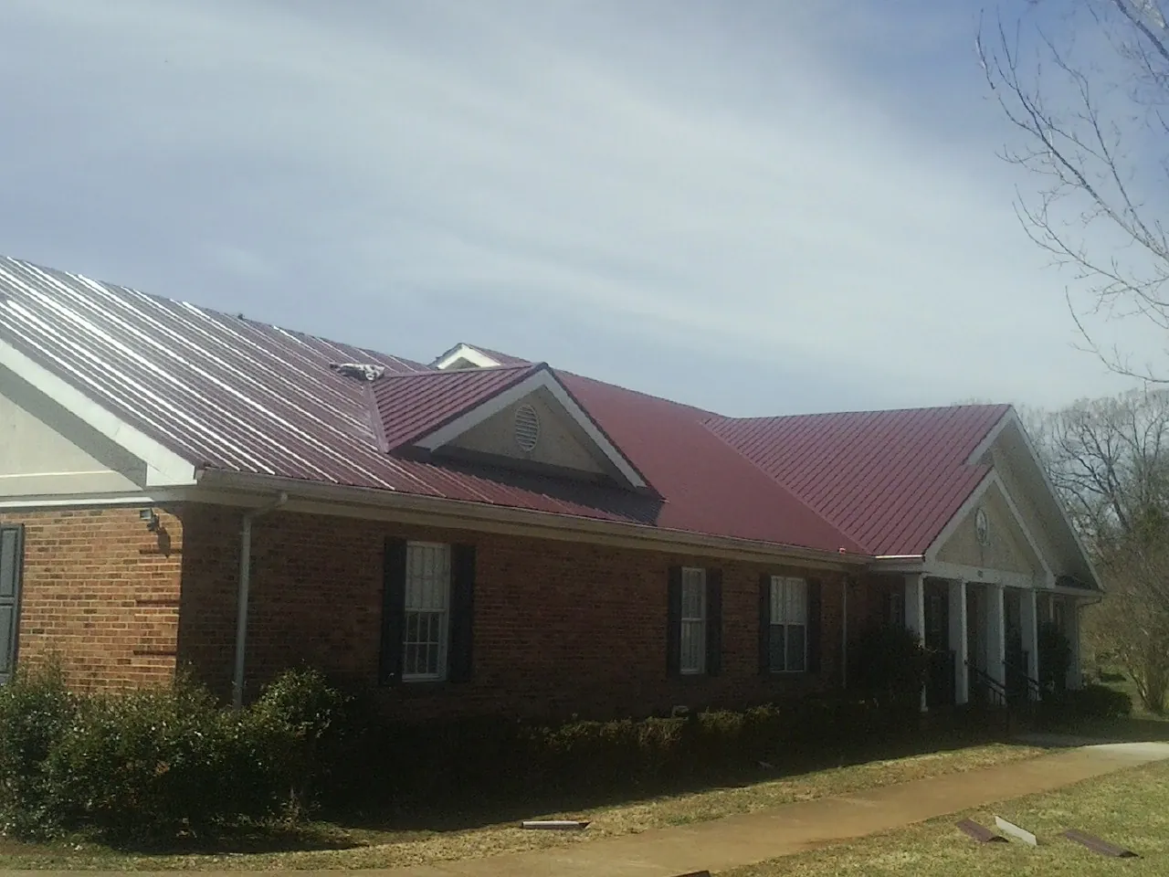 Red metal roof with gabled entries on a long brick building, from a Hail Damage Roof Repair job in Plymouth