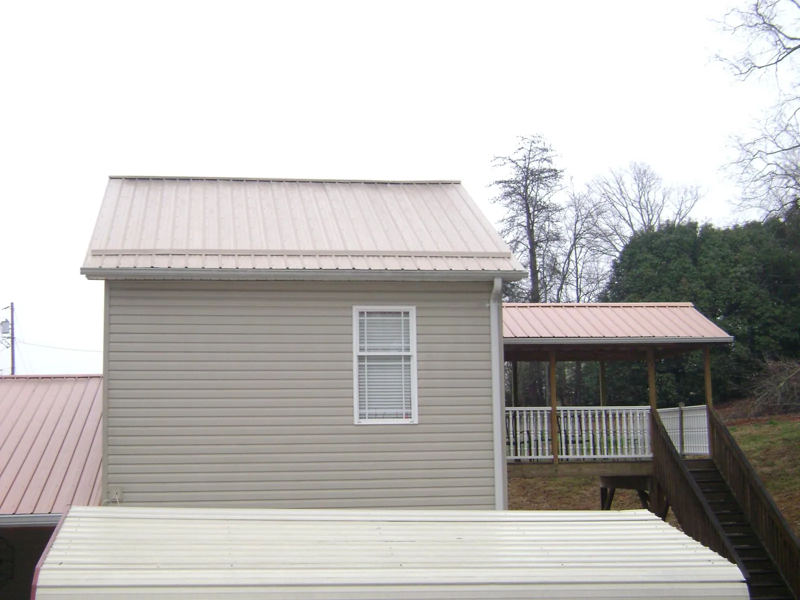 Tan metal roofs on a two story addition and attached porch, from a Roof Replacement job in Plymouth